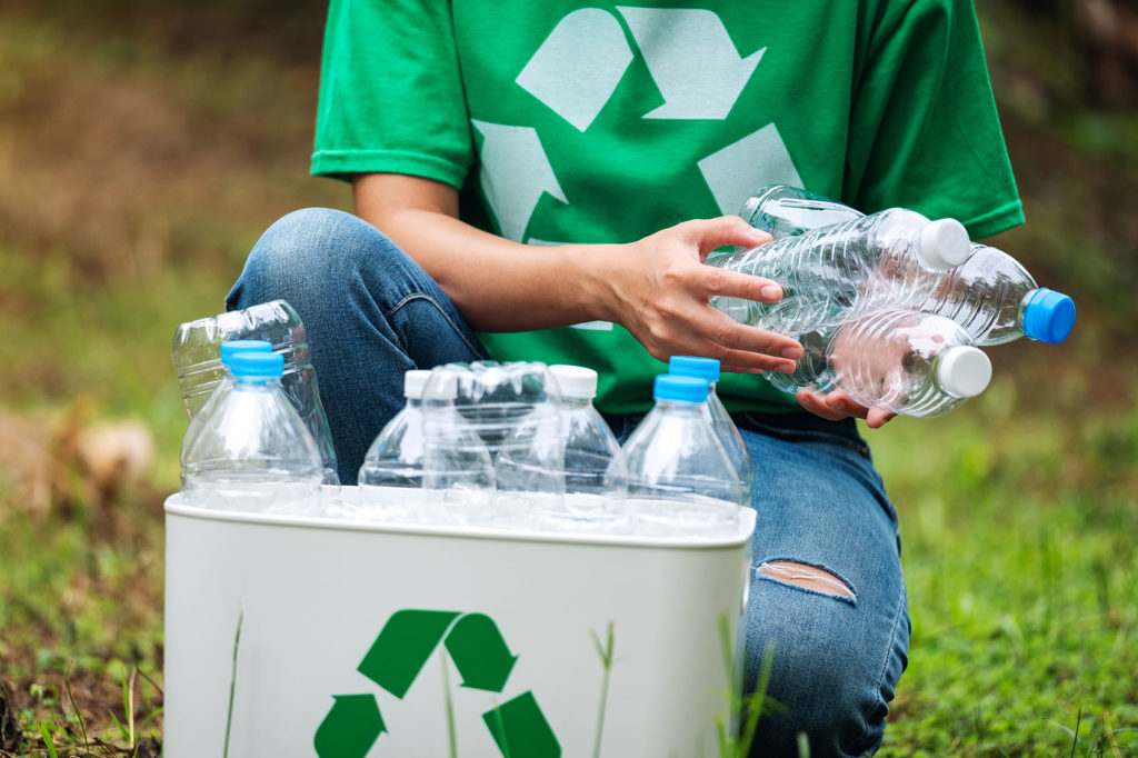 A woman collecting and putting plastic bottles into a recycle bin in the outdoors