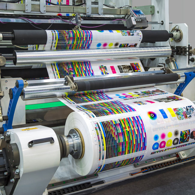 Large offset printing press or magazine running a long roll off paper in production line of industrial printer machine.